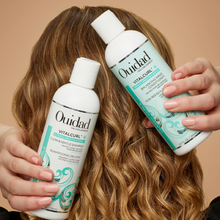 Cargar imagen en el visor de la galería, Modelo cargando Botellas de Acondicionador Ouidad VitalCurl Plus Balancing Rinse 250ml para equilibrar e hidratar rizos.